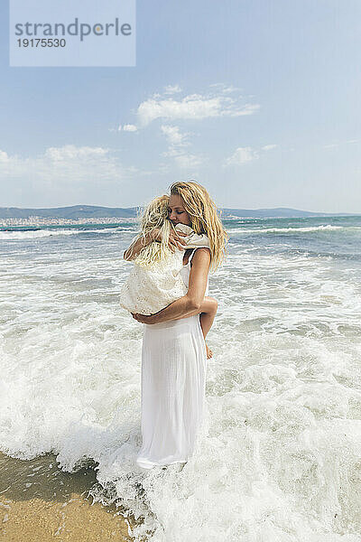 Mutter umarmt Tochter am Strand