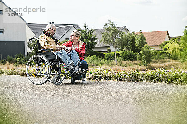 Woman talking with senior man sitting in wheelchair on road