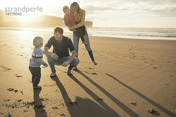 Lächelnder Mann und Frau spielen mit Kindern am Strand
