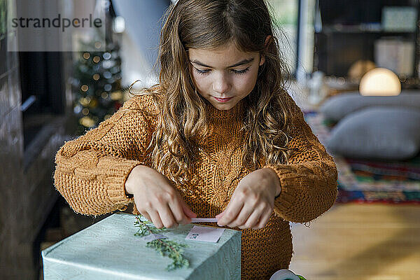 Mädchen klebt zu Hause Namensschild auf Weihnachtsgeschenk