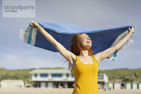 Glückliche Frau mit Schal  die im Urlaub am Strand genießt