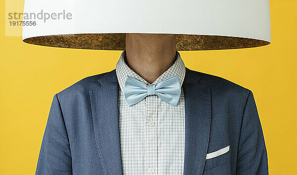 Young man with bow tie hiding face under lamp