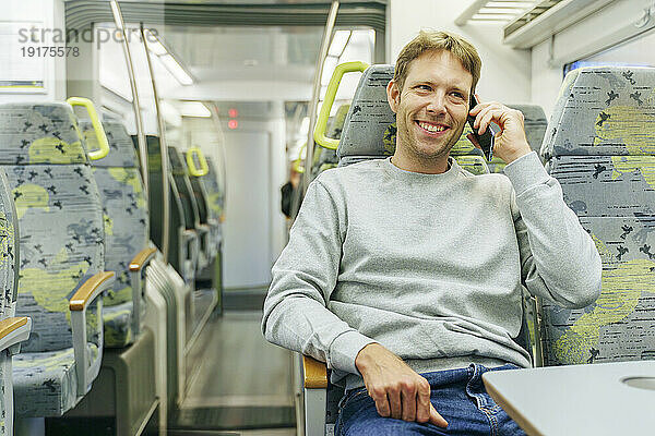 Glücklicher Mann  der im Zug mit dem Smartphone spricht