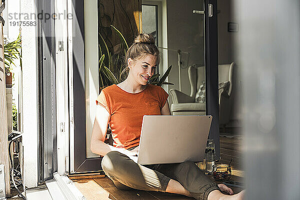 Porträt einer Frau  die mit Laptop am offenen Balkon sitzt