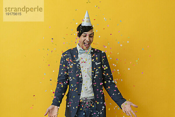 Cheerful man enjoying with confetti against yellow background