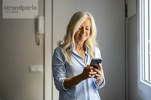 Lächelnde blonde Frau  die zu Hause ihr Smartphone benutzt