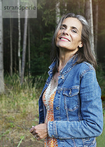 Smiling mature woman in denim jacket at forest