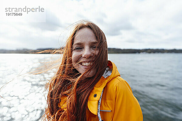 Smiling redhead woman with long hair in front of lake