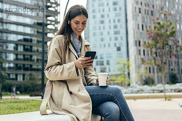 Glückliche Frau  die ihr Mobiltelefon vor Gebäuden benutzt