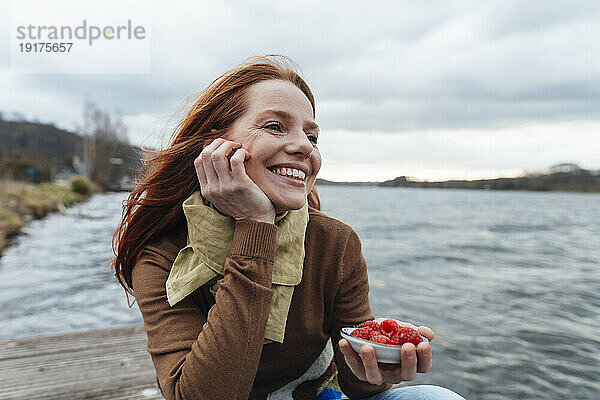 Thoughtful woman with raspberries sitting by lake
