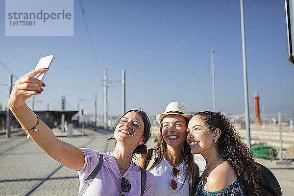 Glückliche Frau  die an einem sonnigen Tag ein Selfie mit Freunden per Smartphone macht
