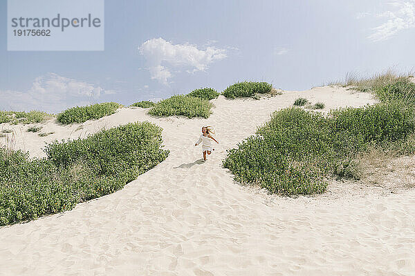 Glückliches Mädchen  das an einem sonnigen Tag in der Nähe von Büschen am Strand läuft