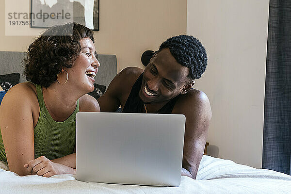 Smiling couple lying on bed with laptop at home