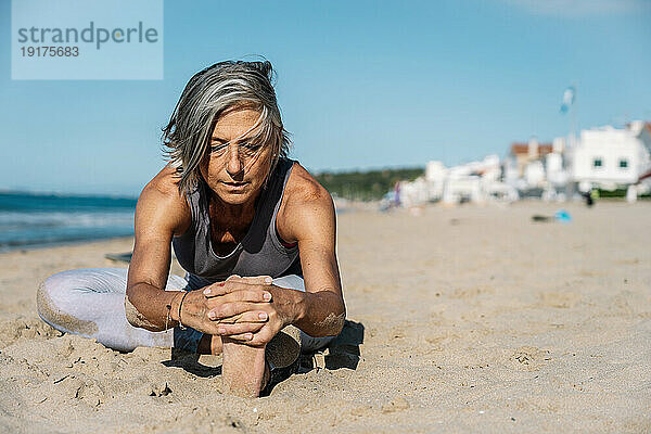 Reife Frau dehnt sich im Sand am Strand