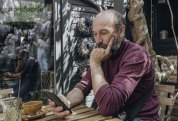 Reifer Mann benutzt Smartphone am Tisch im Straßencafé