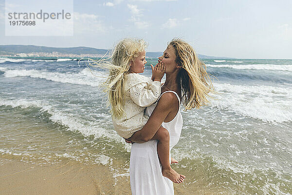 Mädchen berührt Mutters Wangen am Strand