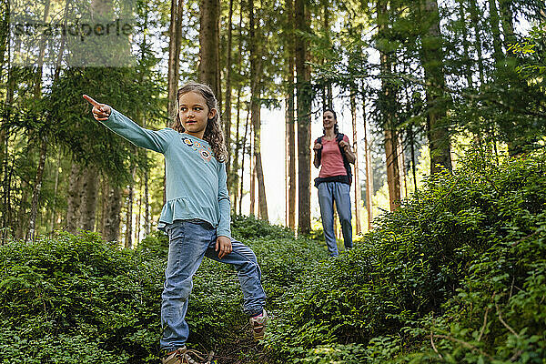 Mädchen zeigt und Mutter läuft von hinten im Wald