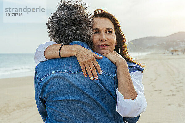Glückliche ältere Frau umarmt Mann am Strand