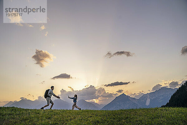 Mädchen rennt auf Vater zu  der auf einer Wiese am Bergmassiv steht