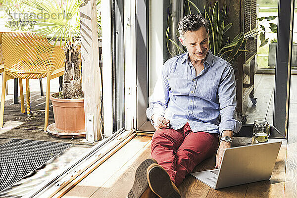 Porträt eines Mannes mit Laptop am offenen Balkon