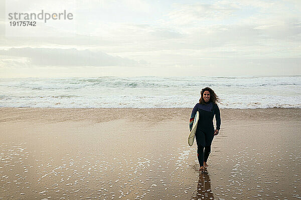 Smiling woman walking with surfboard at beach