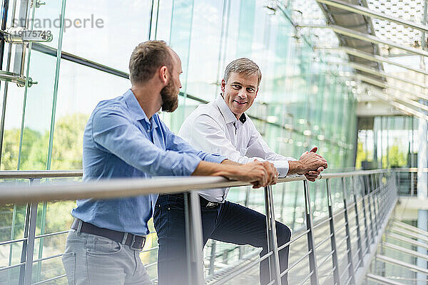 Colleagues talking in office building leaning on railing