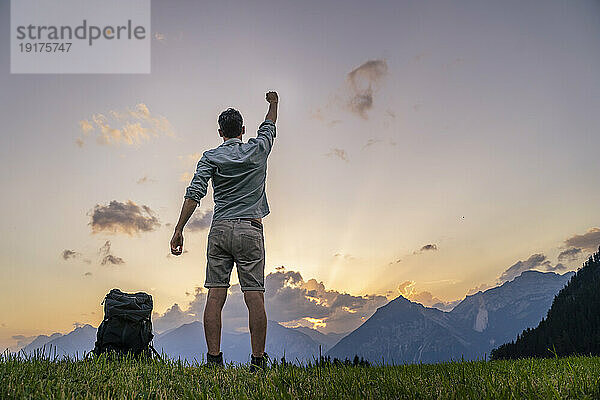 Man with hand raised standing in meadow at sunset