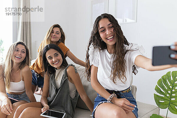 Lächelnde Freunde  die zu Hause auf dem Sofa sitzend ein Selfie machen
