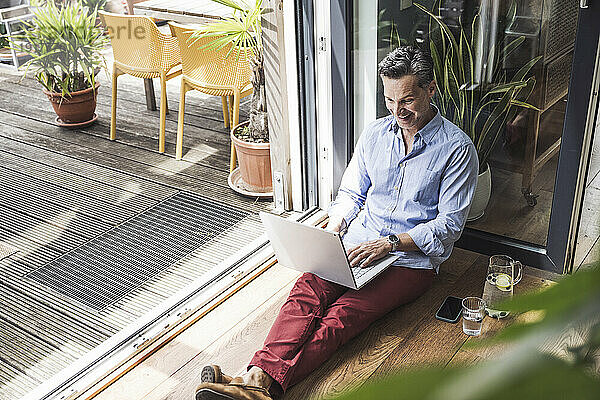 Portrait of man smiling while using laptop by open balcony