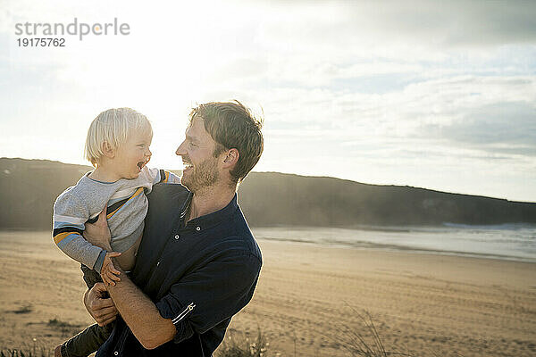 Cheerful father and son at beach on sunny day