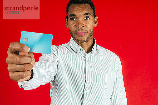 Mann zeigt Kreditkarte vor rotem Hintergrund