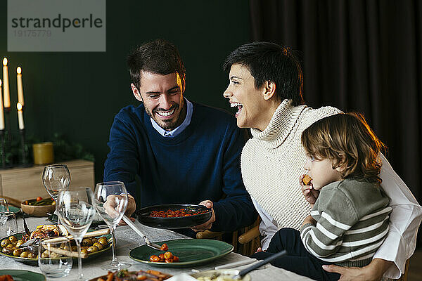 Fröhliche Mutter und Vater mit Sohn beim Abendessen zu Hause an Weihnachten