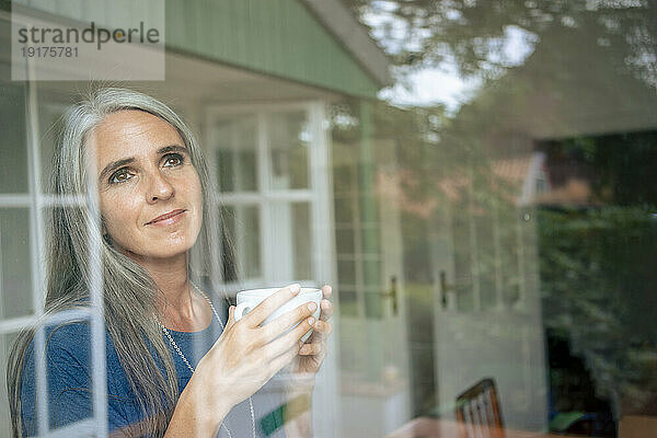 Lächelnde Frau mit Teetasse durch Glas gesehen