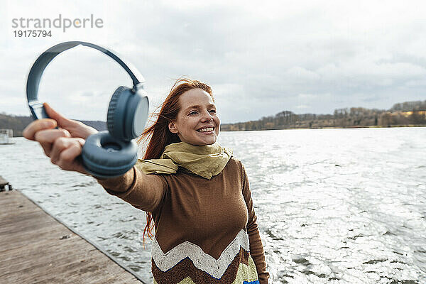 Lächelnde Frau mit kabellosen Kopfhörern am See