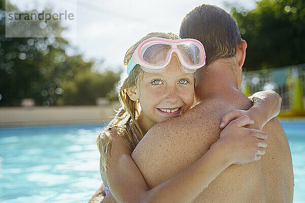 Lächelndes Mädchen mit Schwimmbrille umarmt Vater im Sommer