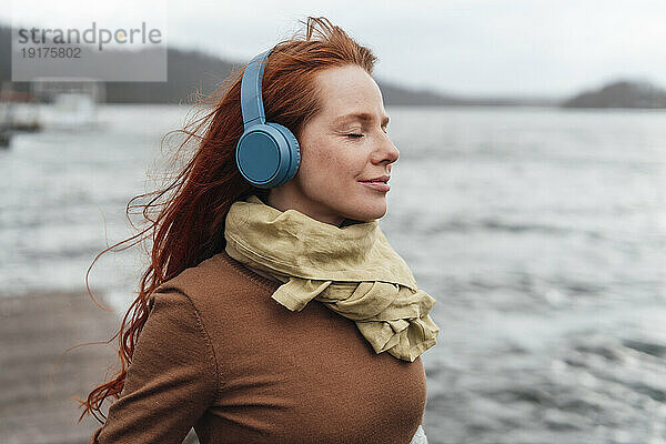 Rothaarige Frau mit geschlossenen Augen  die über kabellose Kopfhörer Musik hört