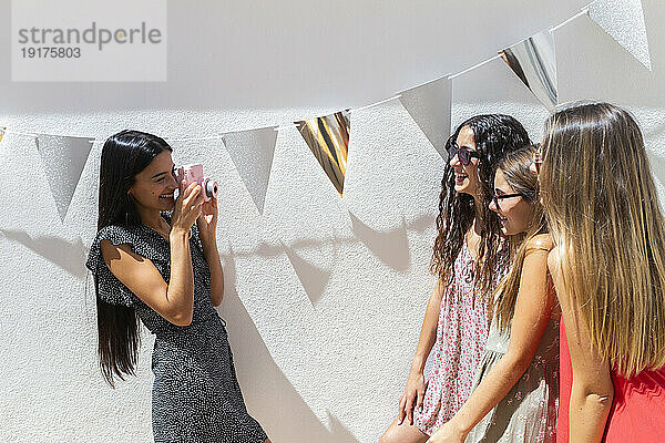 Lächelnde Frau fotografiert Freunde mit der Kamera vor der Wand