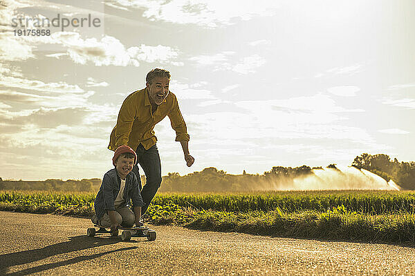 Fröhlicher Junge  der an einem sonnigen Tag mit seinem Großvater Skateboard fährt