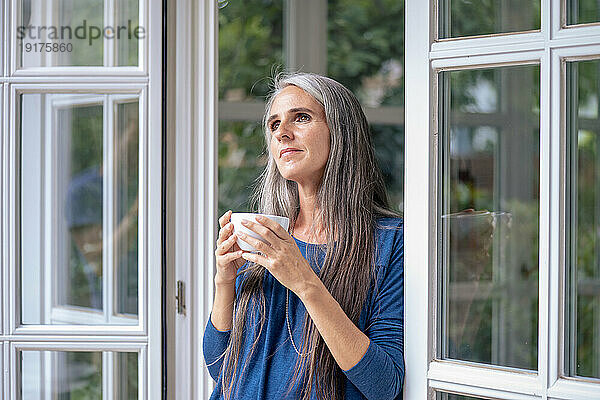 Nachdenkliche reife Frau hält Teetasse im Türrahmen