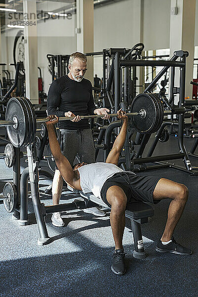 Reifer Trainer hilft Mann beim Krafttraining im Fitnessstudio
