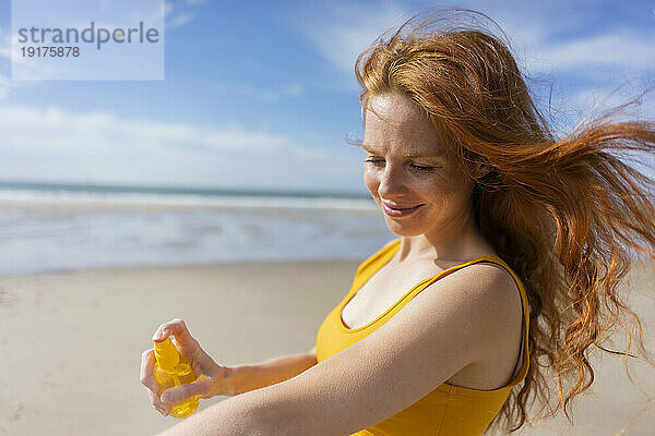 Smiling woman spraying suntan lotion on hand at beach