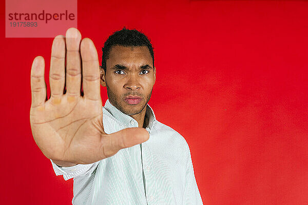 Mann macht Stopp-Geste vor rotem Hintergrund