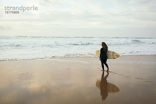Frau mit Surfbrett läuft am Strand in Richtung Meer