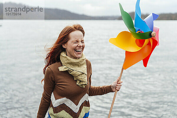 Frau hält Windradspielzeug in der Hand und lacht am See