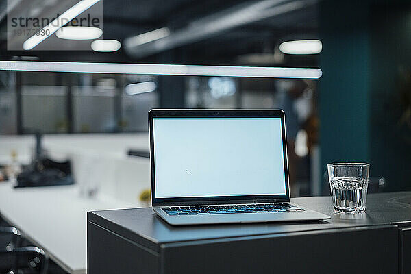 Laptop und Glas Wasser auf dem Schreibtisch im Büro
