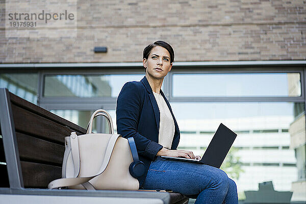 Selbstbewusste Geschäftsfrau sitzt mit Laptop auf der Bank