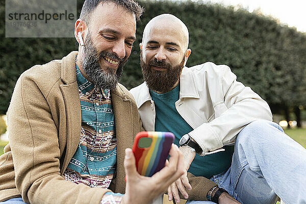 Glücklicher schwuler Mann benutzt Smartphone mit Freund im Park