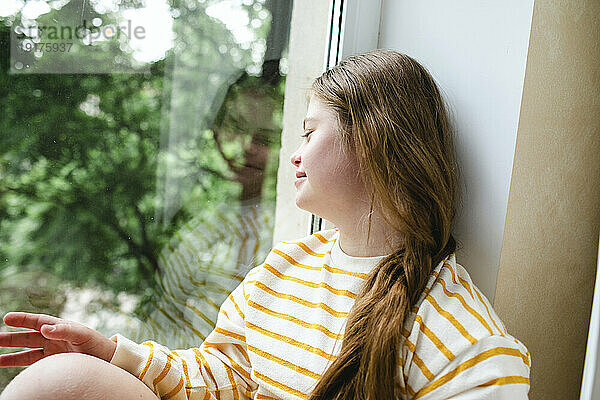 Mädchen mit Down-Syndrom schaut zu Hause durch das Fenster