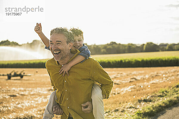 Fröhlicher Mann trägt Enkel huckepack durch das Feld