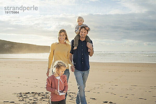 Lächelnder Vater und Mutter  die an einem sonnigen Tag mit Kindern am Strand spazieren gehen